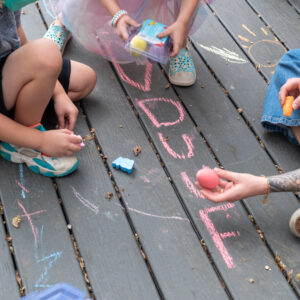 Hands of two children and a teacher drawing DUUF with sidewalk chalk