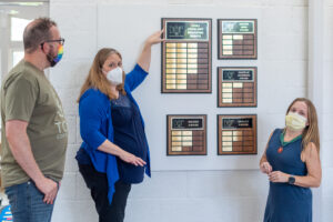 Three members observe the award plaques on the wall of the Fellowship Hall.