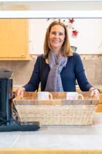 A smiling woman places a basket of coffee mugs on the counter in the kitchen