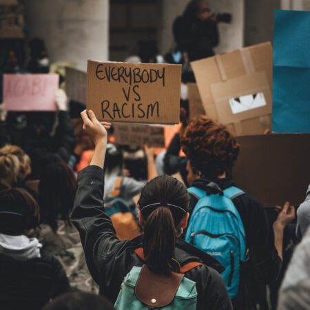 woman in a crowd holding up a sign that reads "everybody versus racism"